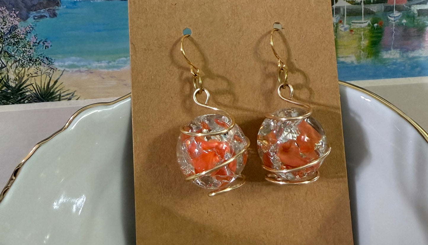 Wire-wrapped orange cracked marble earrings with stainless steel ear wires resting in a bowl displayed on a brown card.