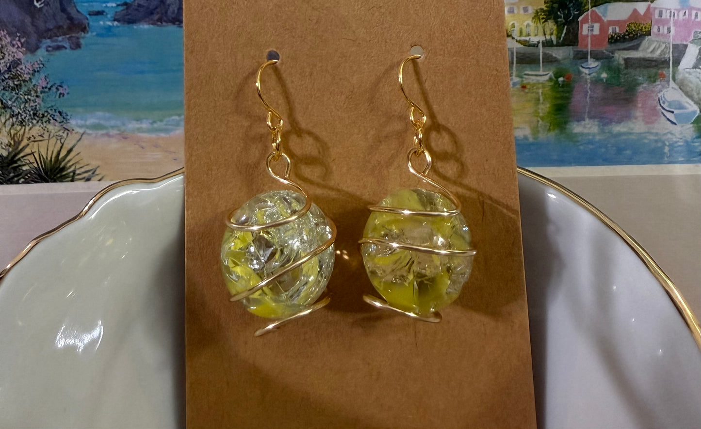 Wire-wrapped yellow cracked marble earrings with stainless steel ear wires resting in a bowl displayed on a brown card.