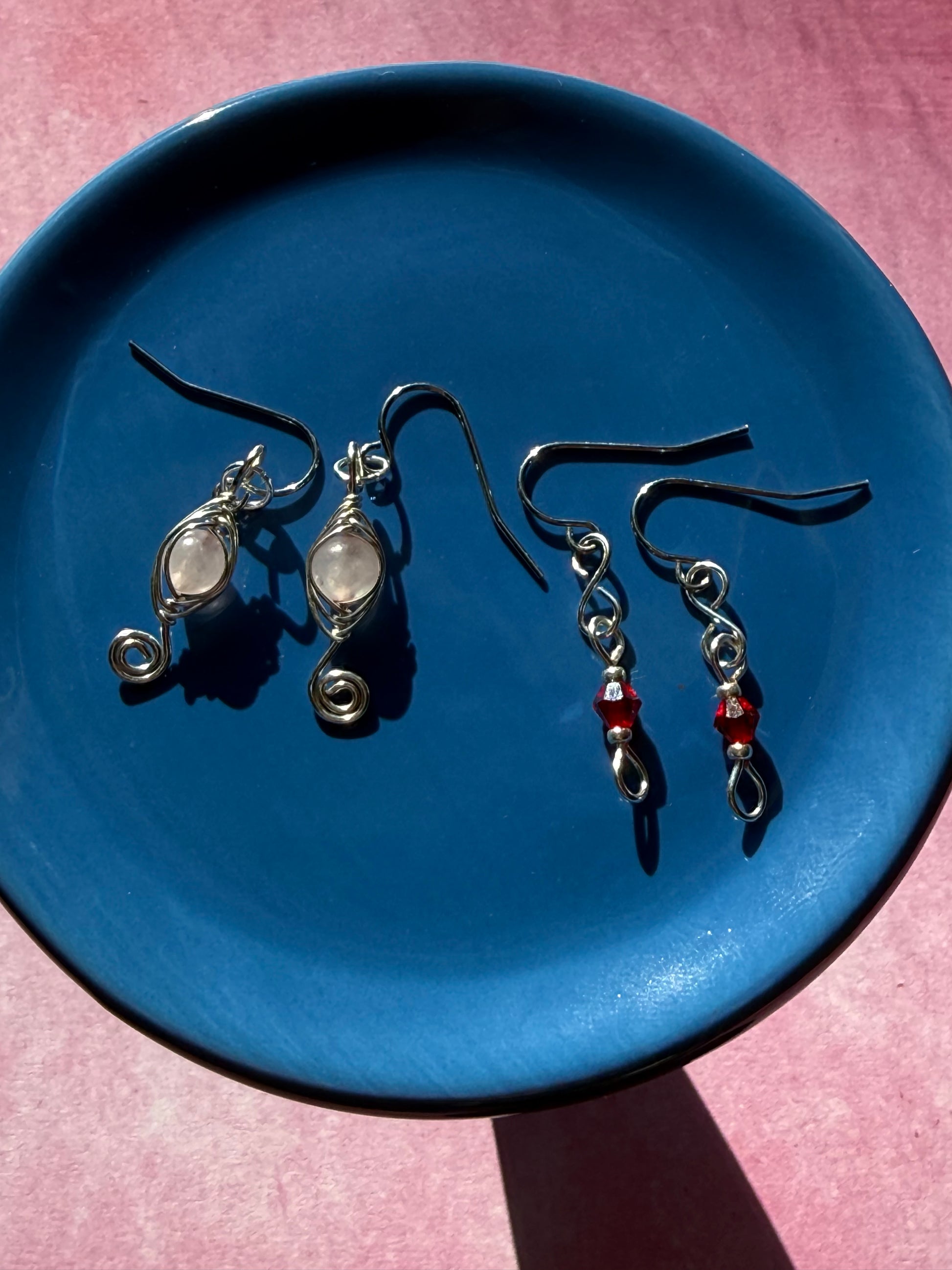 Herringbone wire-wrapped Rose Quartz swirl earrings and red crystal petite earrings on a blue plate.