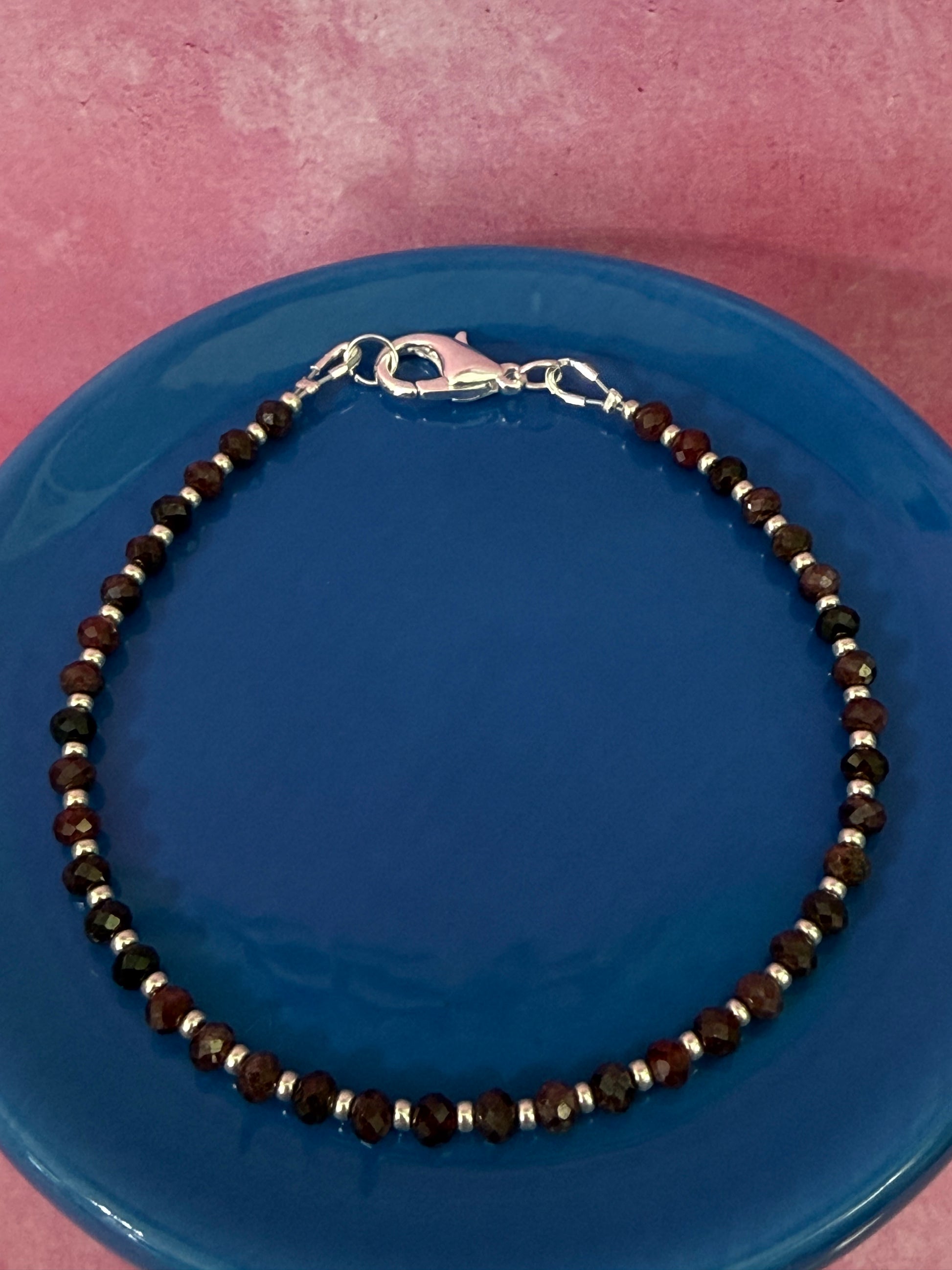 Garnet gemstone and silver seed bead stackable bracelet with a silver-plated brass lobster claw clasp on a blue plate.