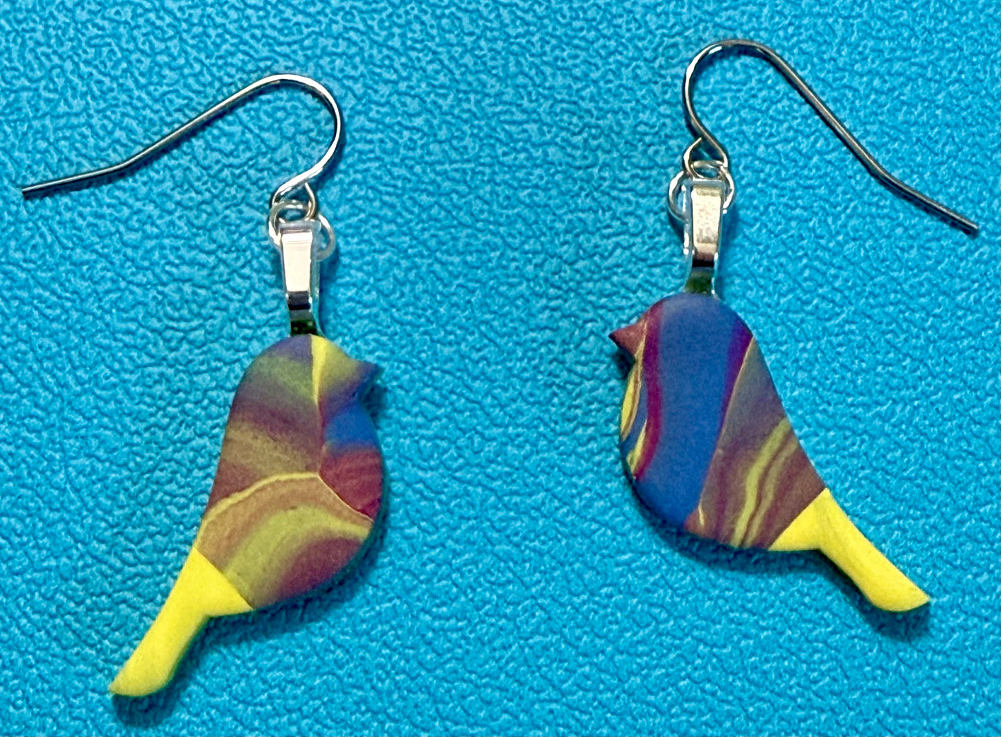 Handcrafted polymer clay bird-shaped earrings in swirled yellow, green, purple, blue, and white tones with stainless steel ear wires