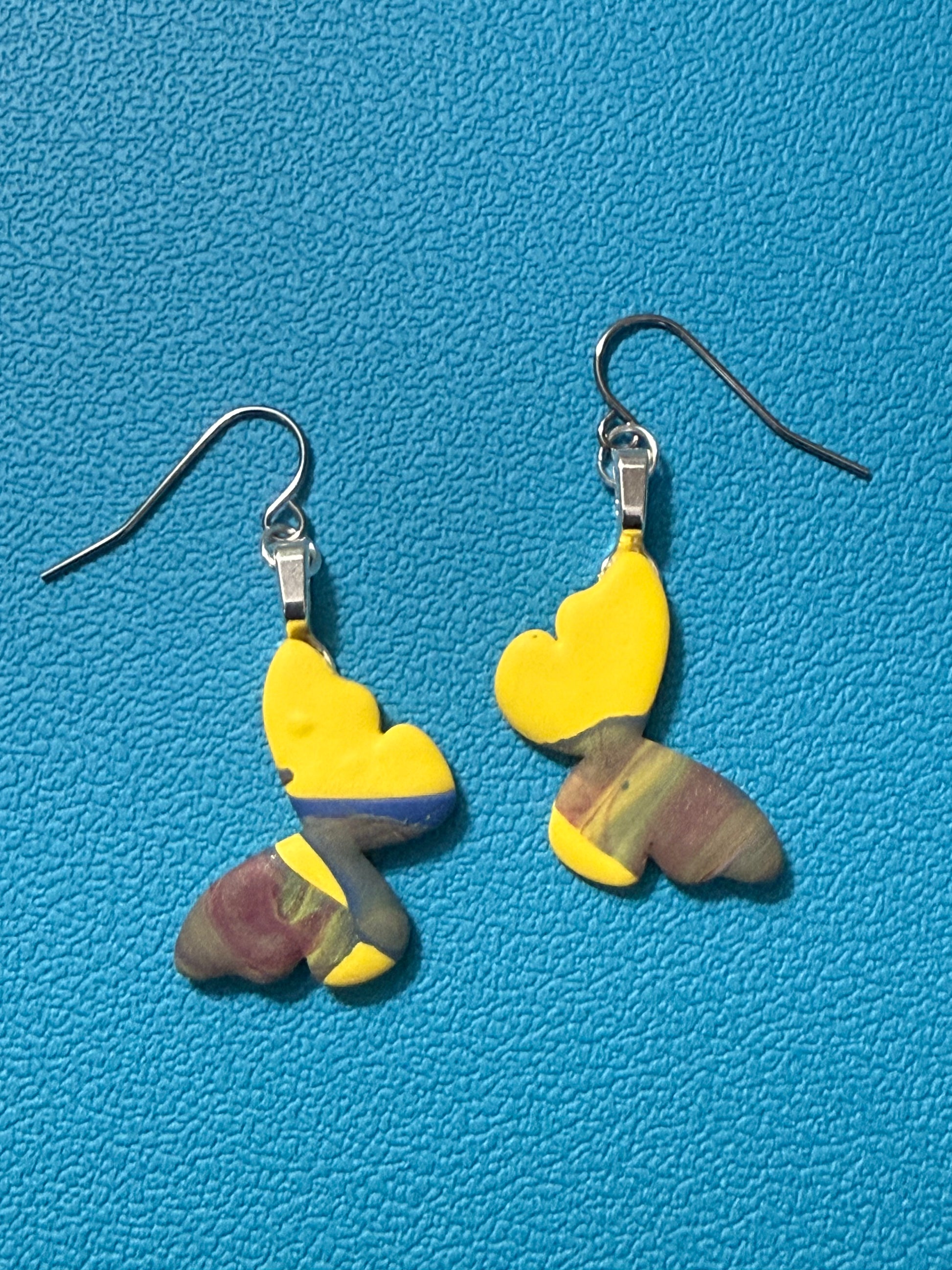 Handcrafted polymer clay butterfly earrings with bright yellow wings and swirled green, purple, blue, and white lower wings, with stainless steel ear wires