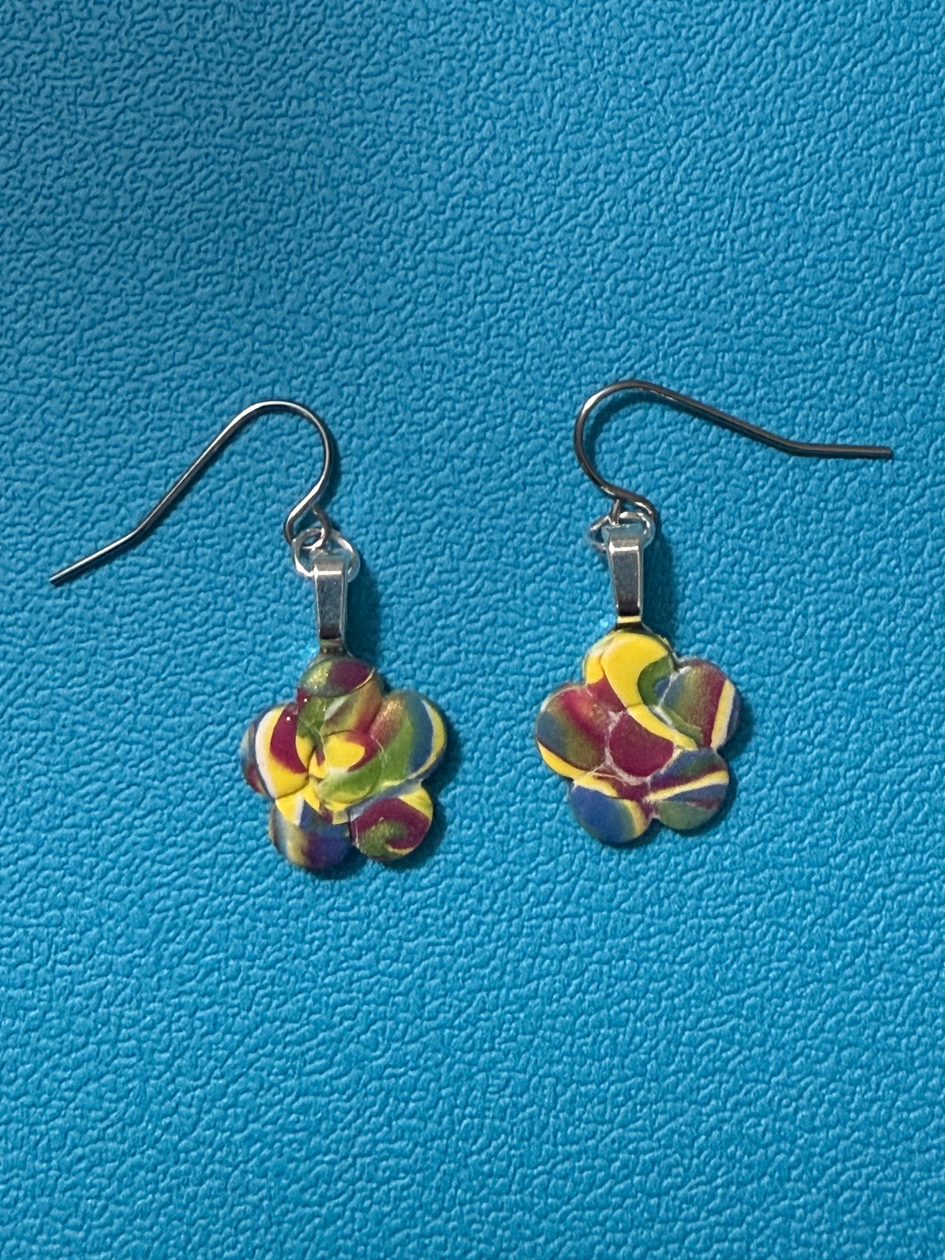 Handcrafted polymer clay flower-shaped earrings in swirled yellow, green, purple, blue, and white tones with stainless steel ear wires