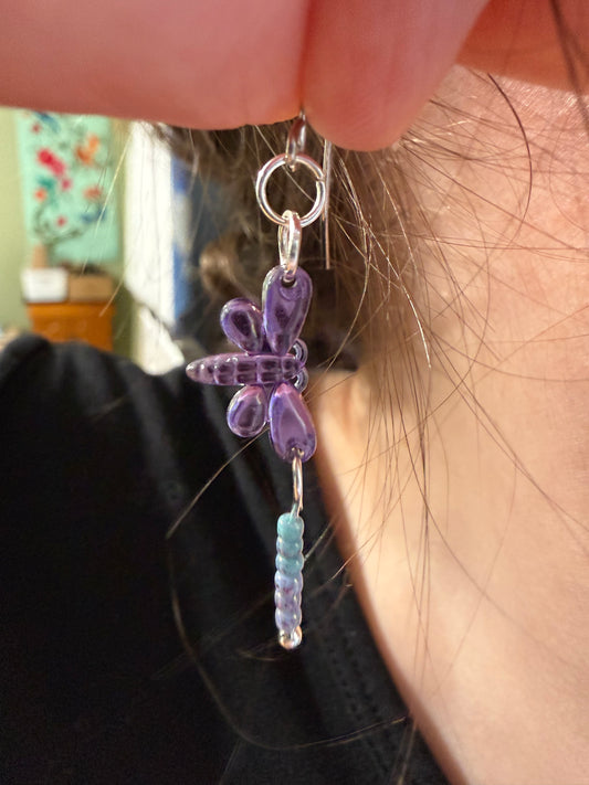 Close-up of an earring with a purple dragonfly sequin charm and a light blue and purple seed bead dangle.