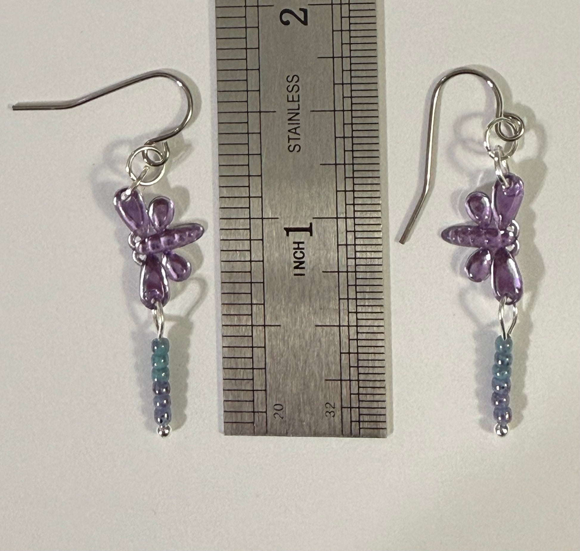 Earrings with purple dragonfly sequin charms and light blue and purple seed bead dangles next to ruler measure about 1.5 inches.
