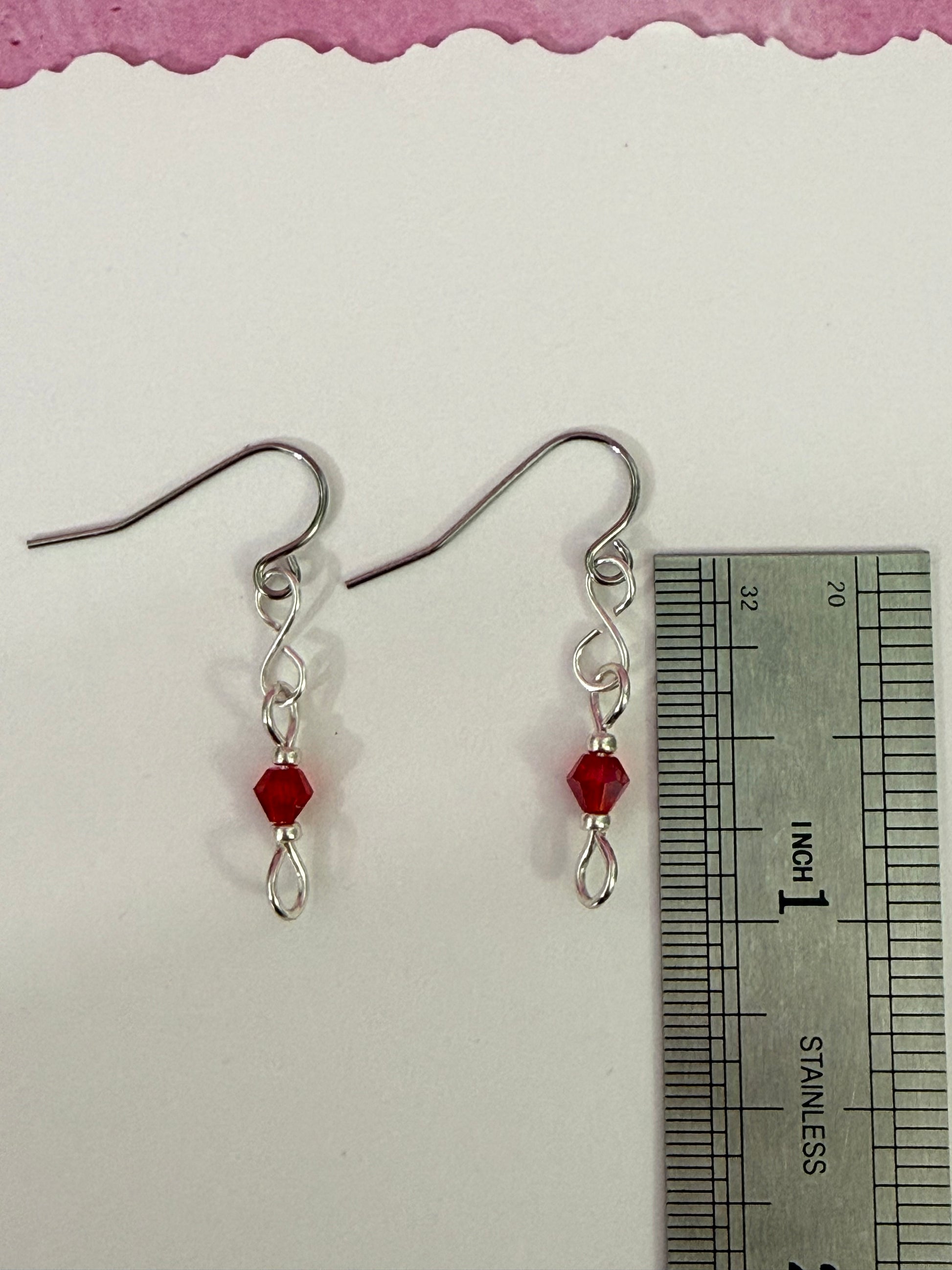 Pair of earrings with red crystal beads and stainless steel ear wires on a white background with a ruler for scale.