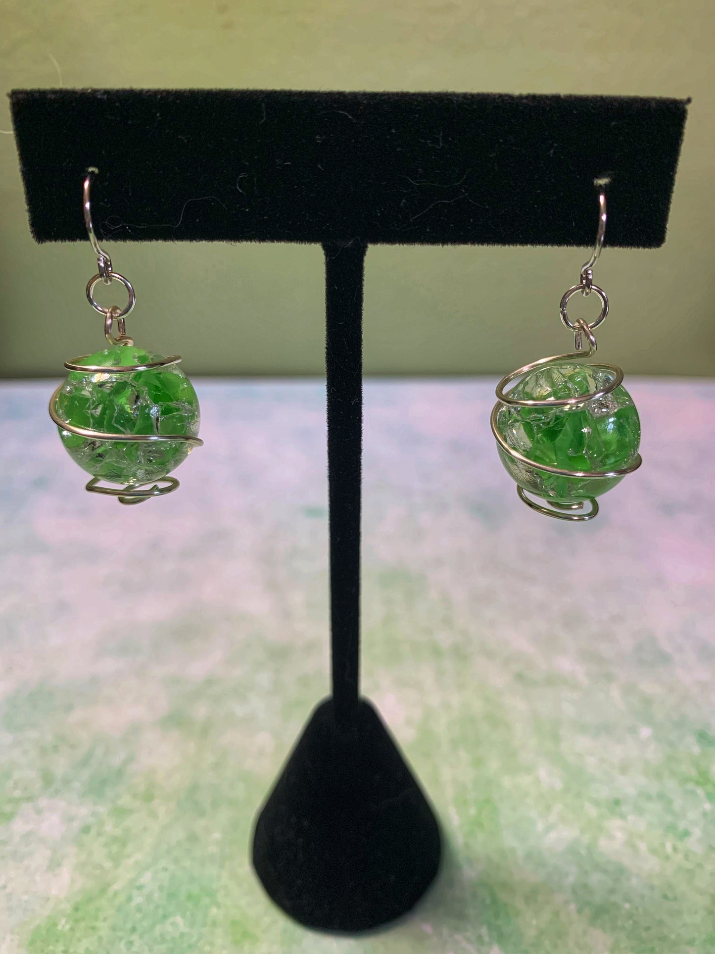 Wire-wrapped green cracked marble earrings with stainless steel ear wires hanging on earring display.
